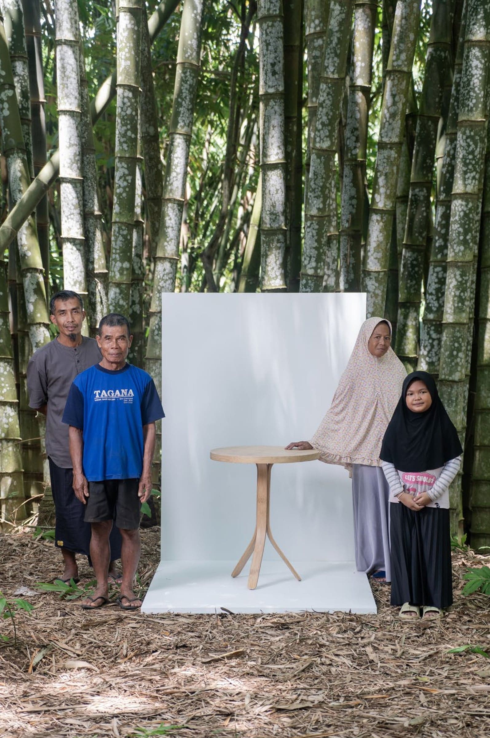 A family of bamboo growers in a grove, standing beside a bamboo side table