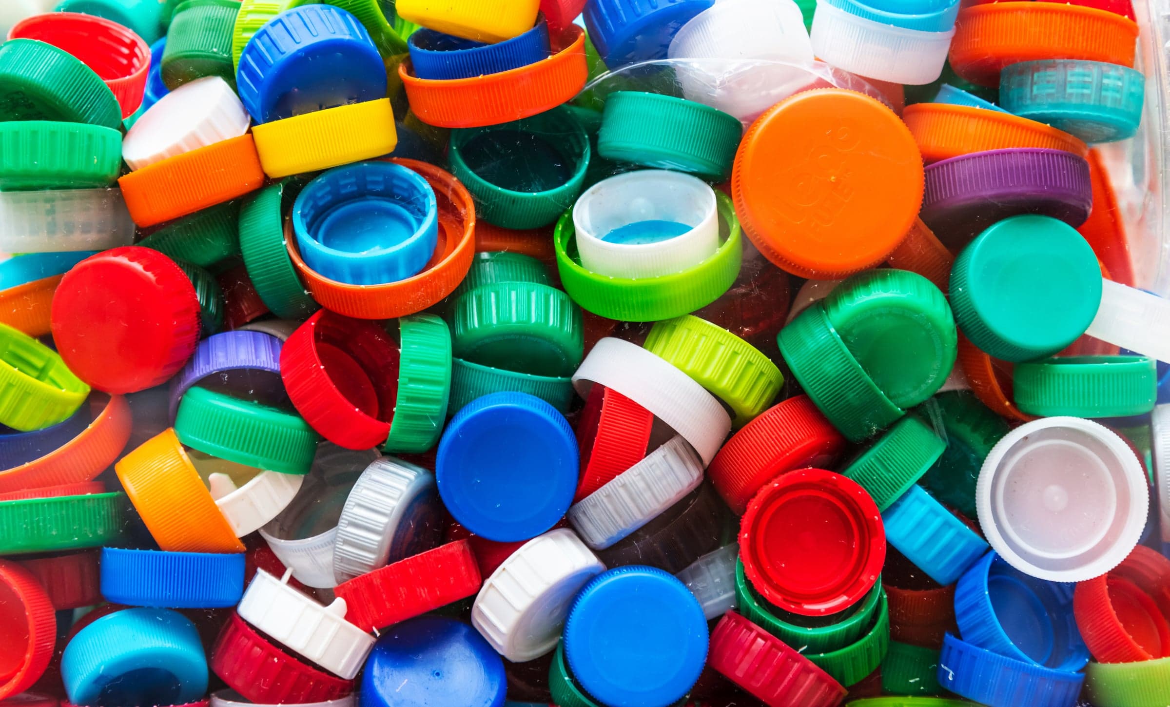 A pile of plastic bottle caps in red, green, blue, orange and white