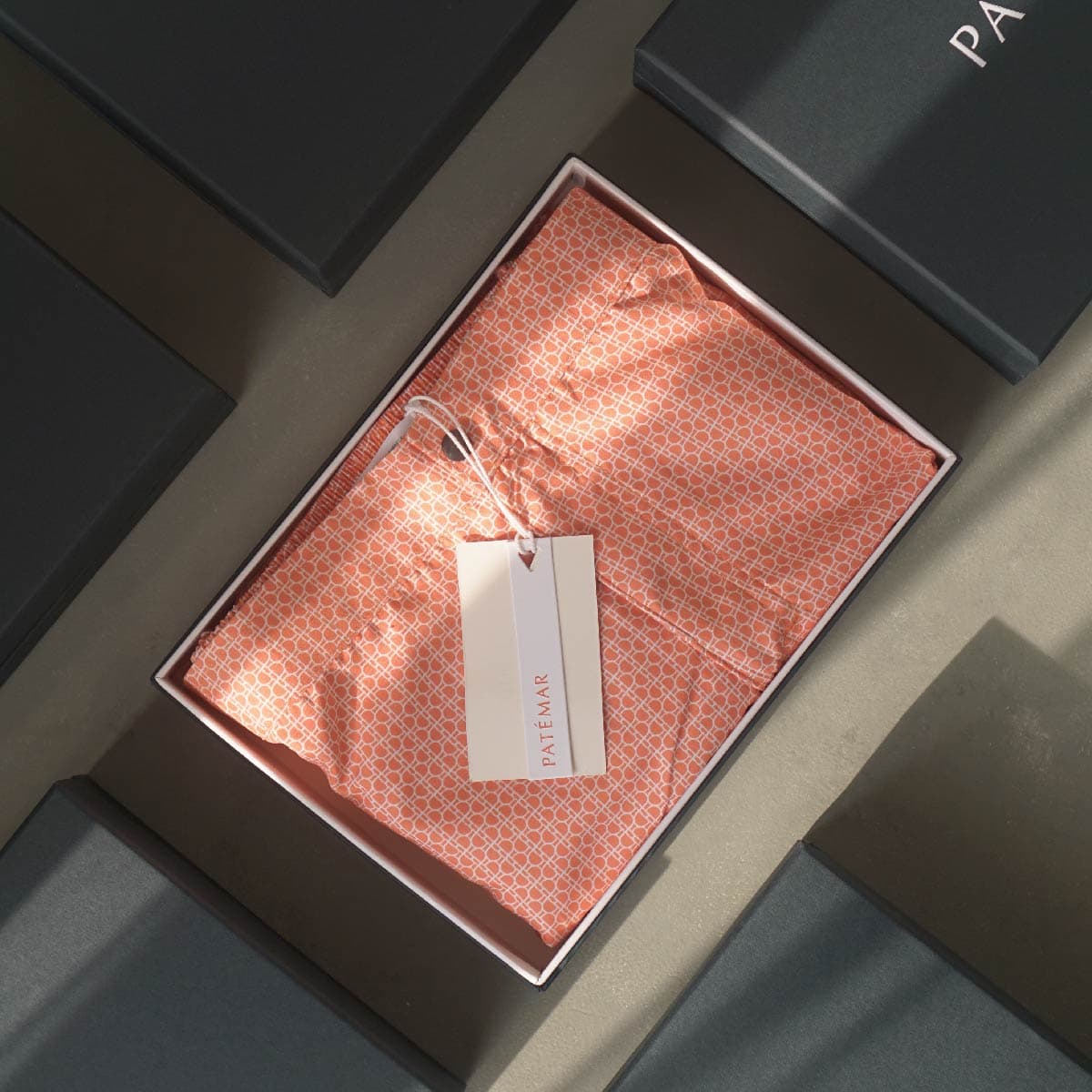 Coral Patémar swim shorts folded in an open gift box, with a Patémar tag