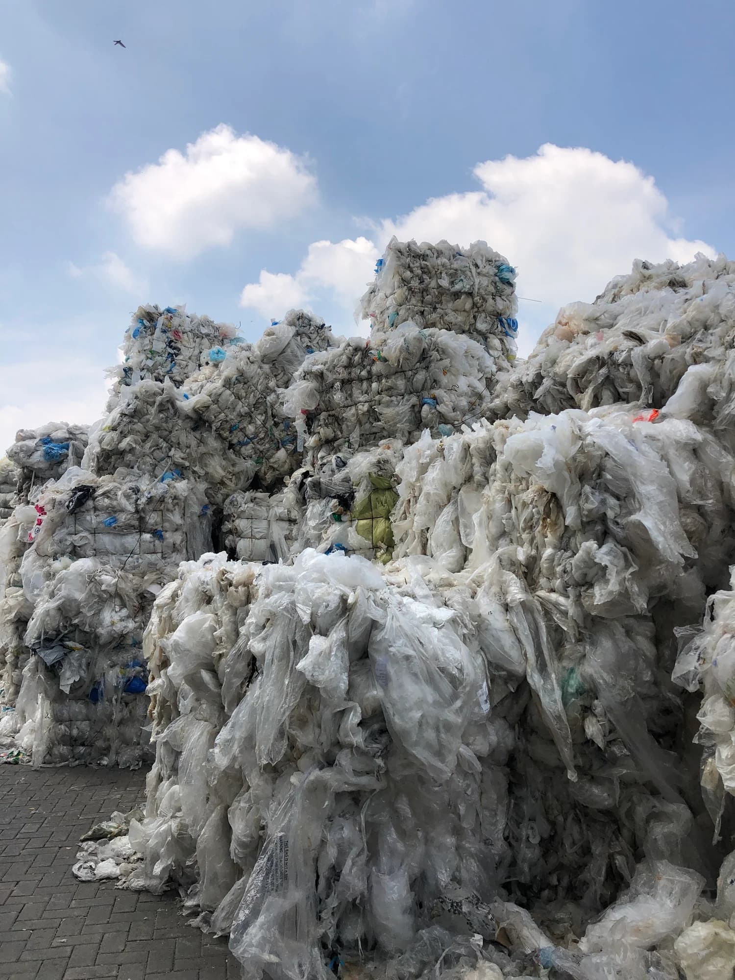 Bales of compressed plastic waste stacked high under a blue sky