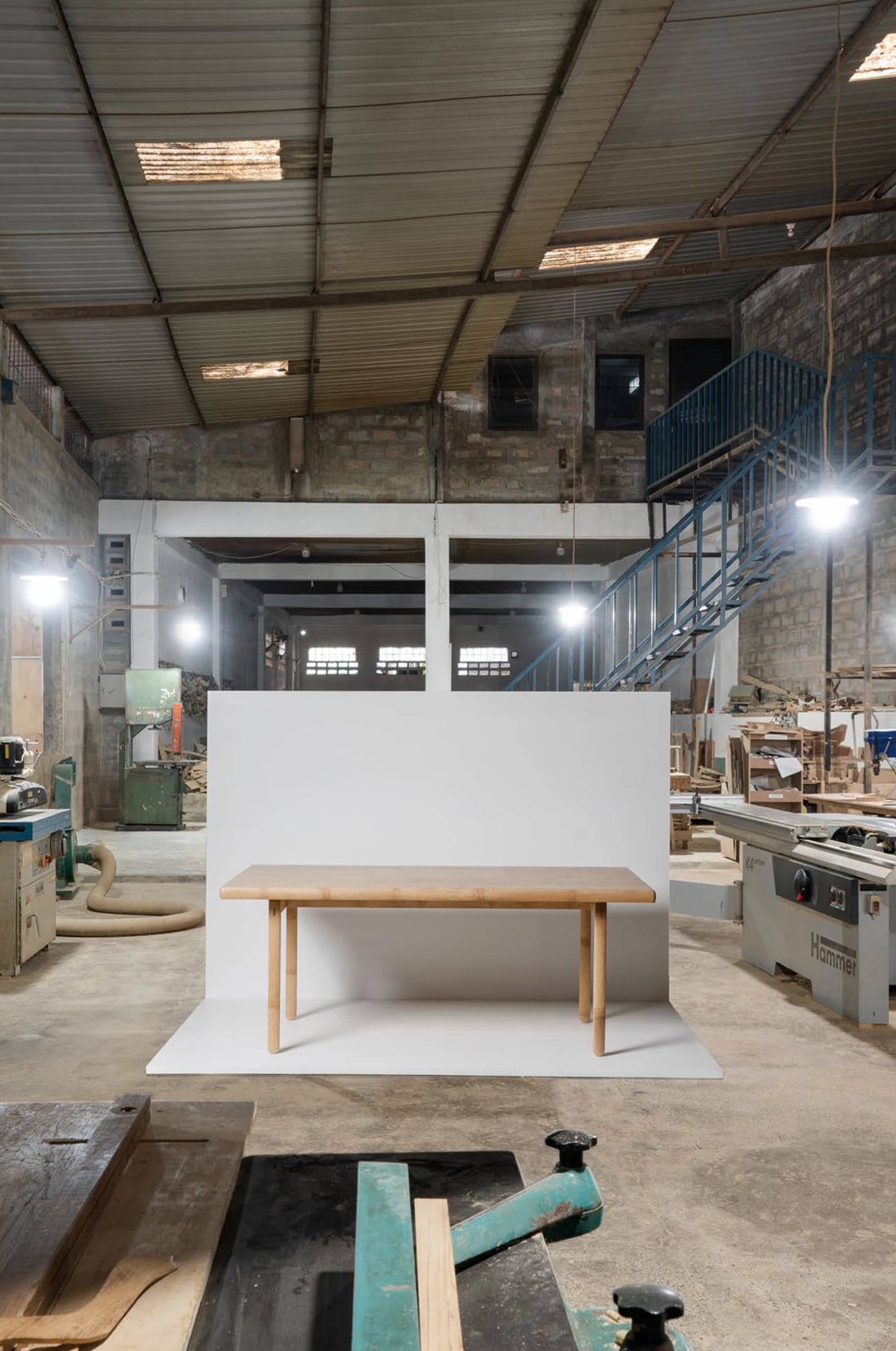 A bamboo table set in front of a white board inside a furniture workshop